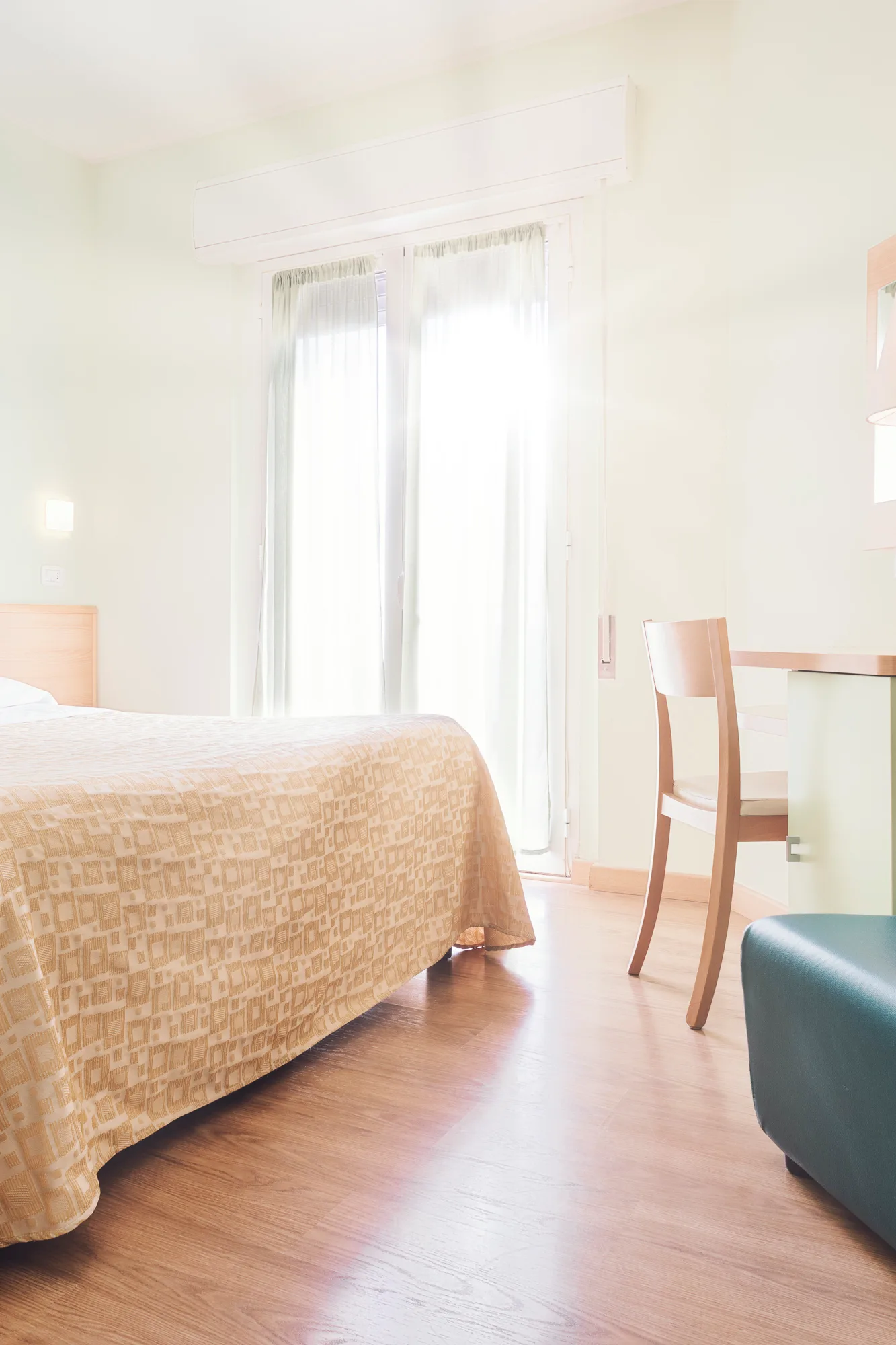 Stanza illuminata con porzione di letto, sedia e divano