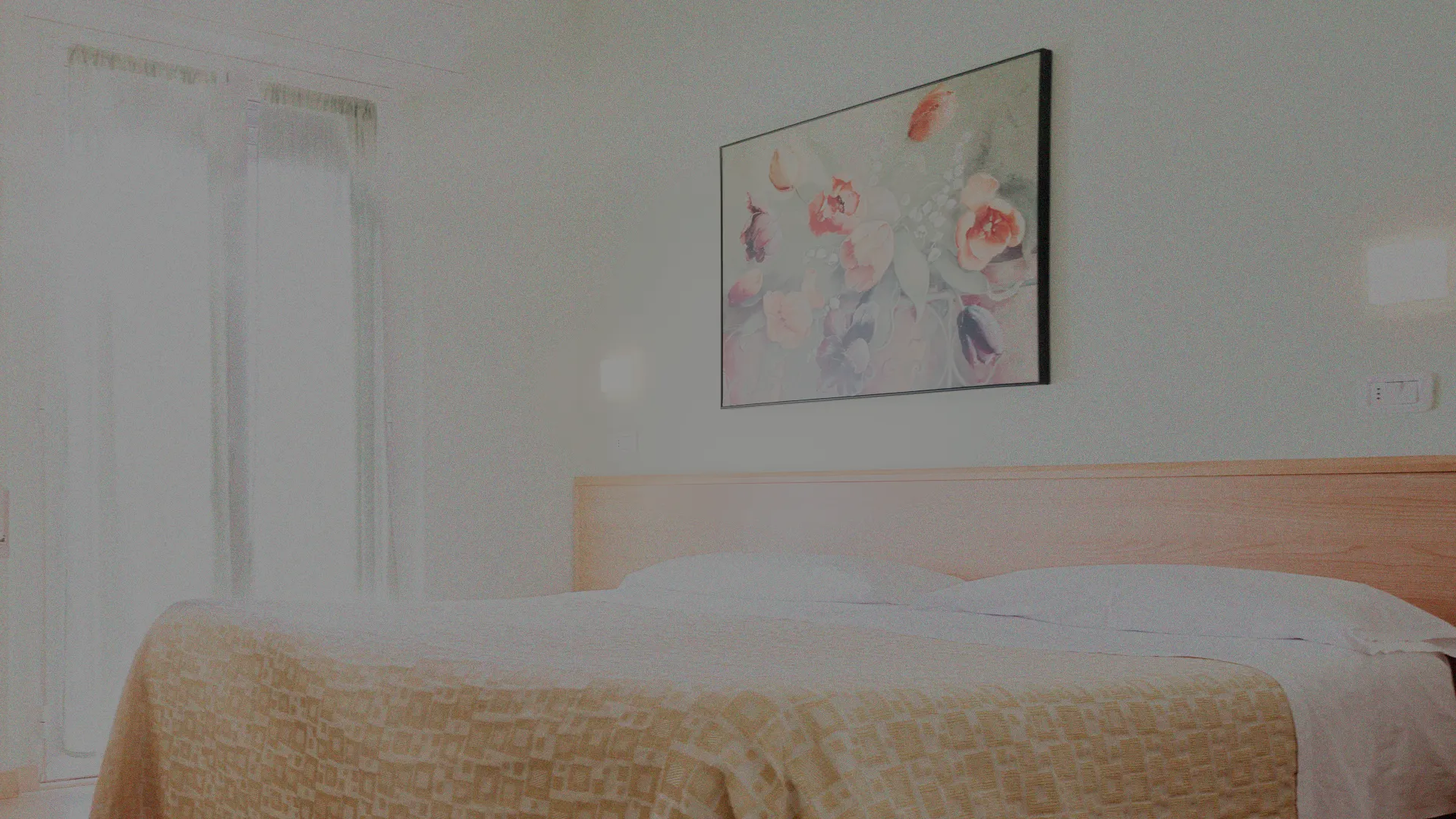 Uno scatto di una camera illuminata dell'hotel raffigurante un letto, un divano, un comodino con telefono e una finestra.